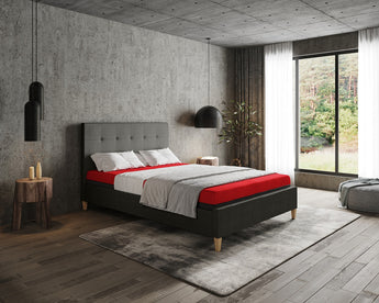 Modern bedroom with a gray upholstered bed, red Thevo mattress, and concrete walls.