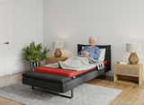 Man lying on a Thevo bed in a modern bedroom with wooden nightstands and lamps.