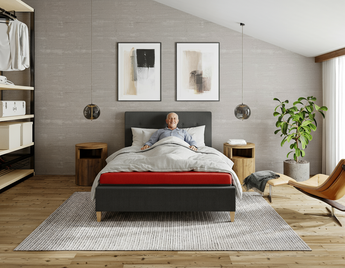 Man lying in therapeutical Thevo bed in a modern bedroom with gray walls, wooden floor, and decorative elements.